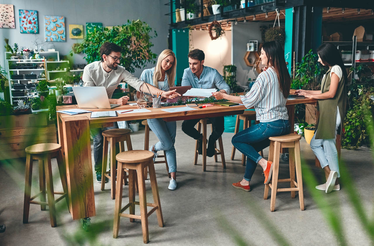 Na obrázku sú ľudia v coworkingu. Historicky slovo coworking malo etymologický význam „spolupráca”.